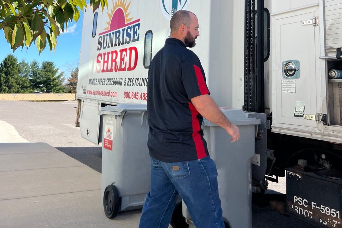 Sunrise Shred driver rolling a locked shred bin to the truck